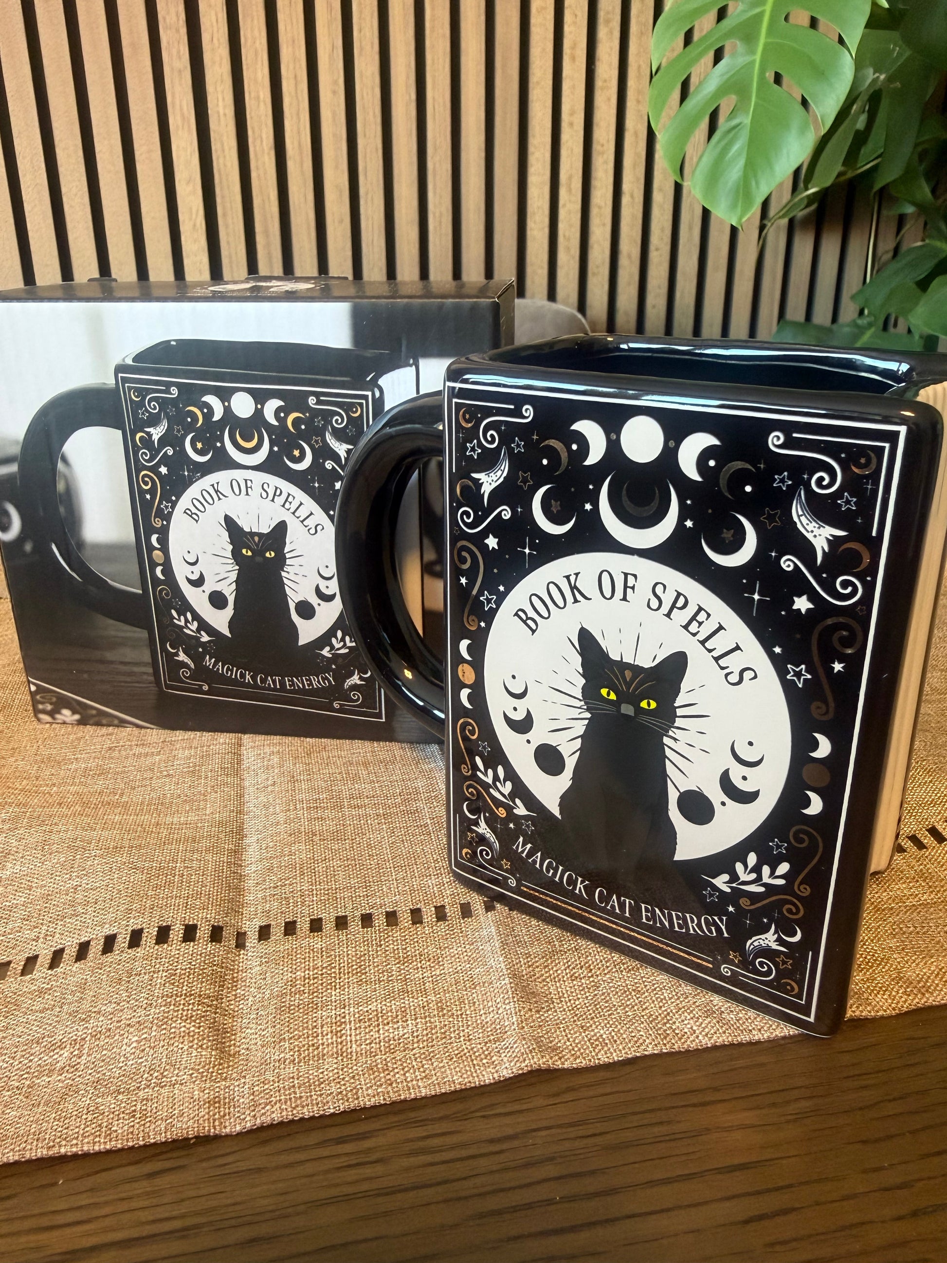 Book-shaped black ceramic mug with Book of Spells Magick Cat Energy design featuring moon phases and black cat