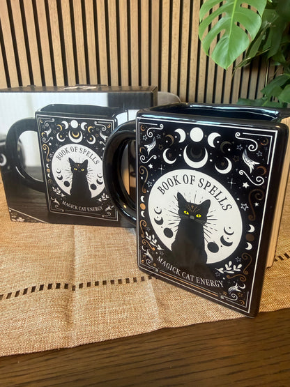 Book-shaped black ceramic mug with Book of Spells Magick Cat Energy design featuring moon phases and black cat